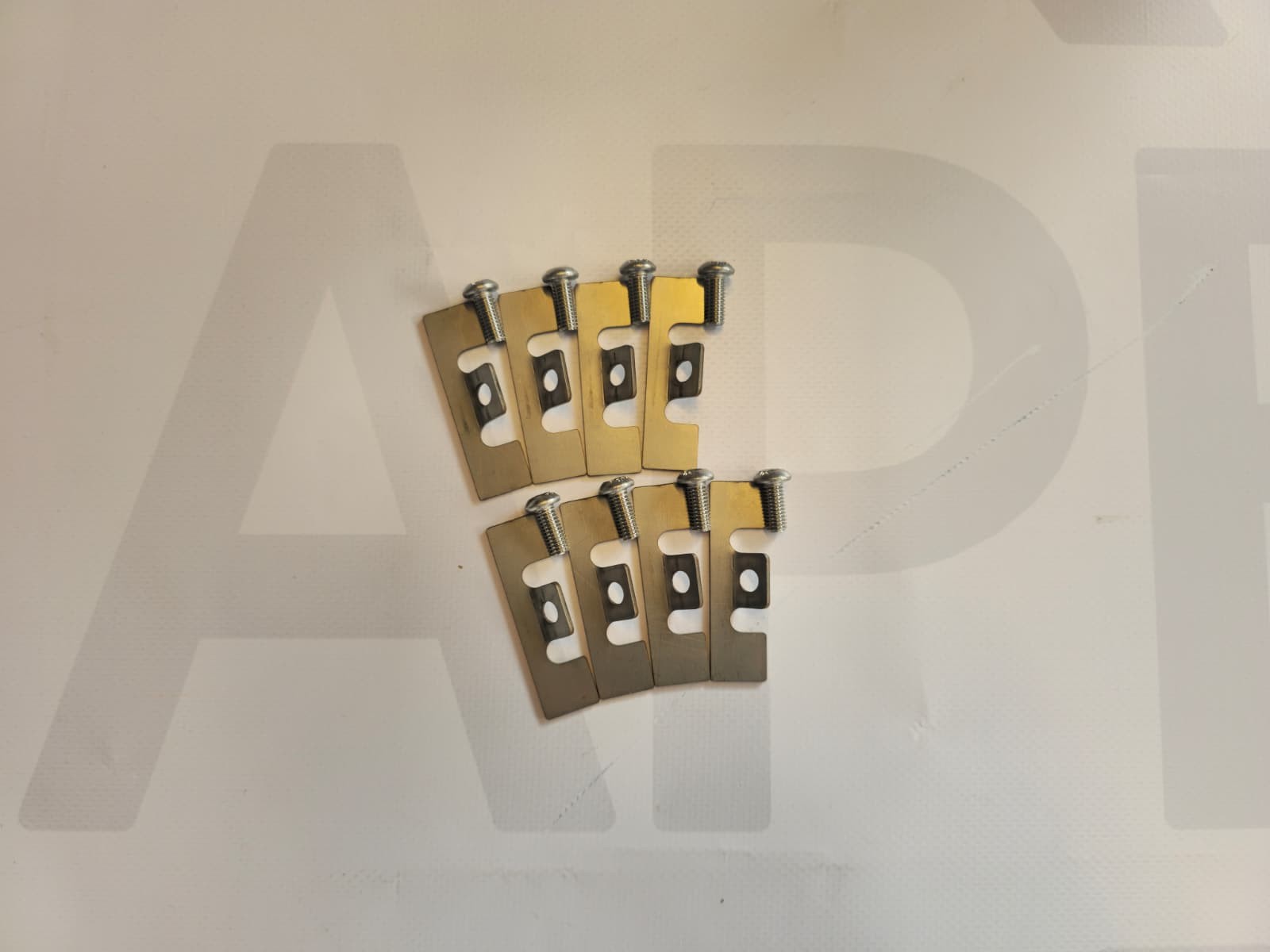 Eight metal clips with screws on a white surface