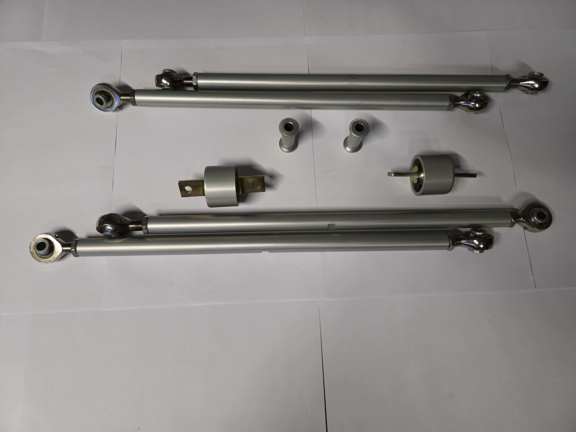 Componentes metálicos incluindo braços telescópicos, cilindros e adaptadores sobre superfície branca