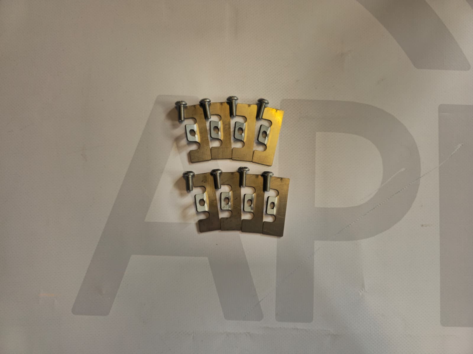 Eight small metallic bracket plates with screws on a white surface.