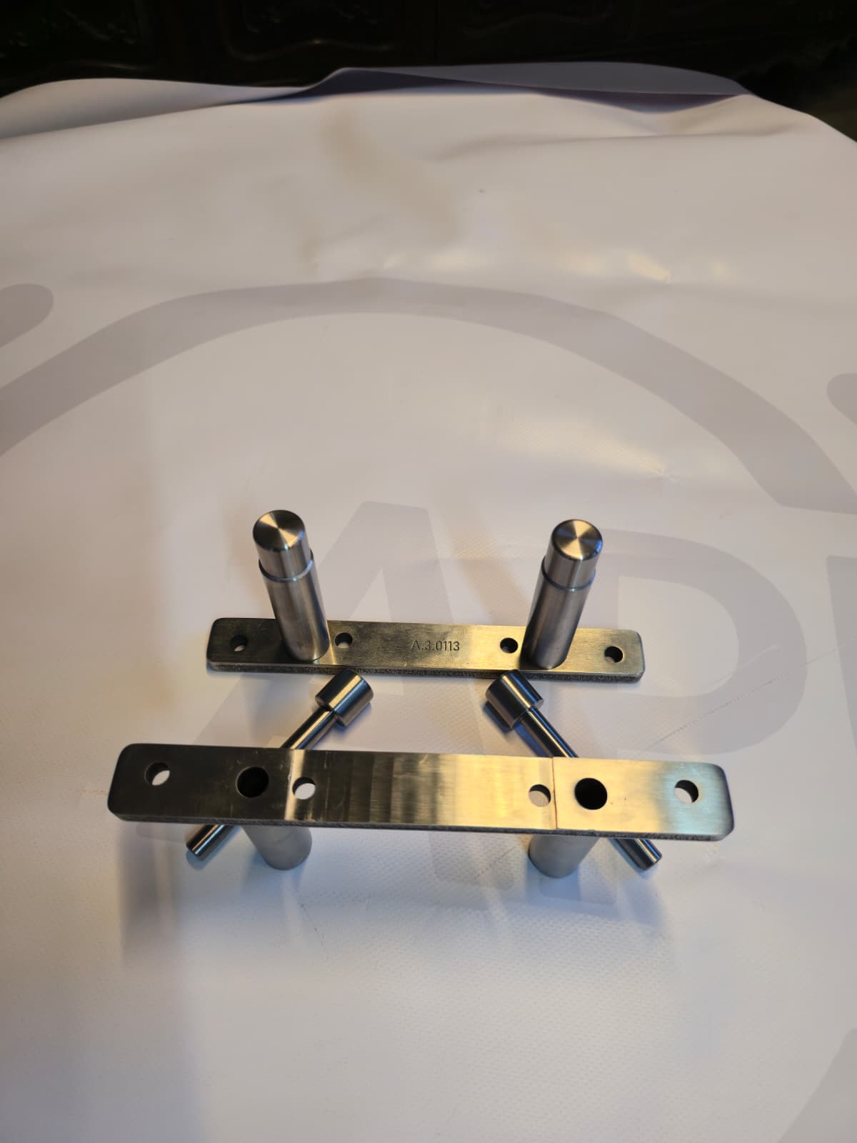Two metallic mounting brackets with cylindrical pegs on white surface