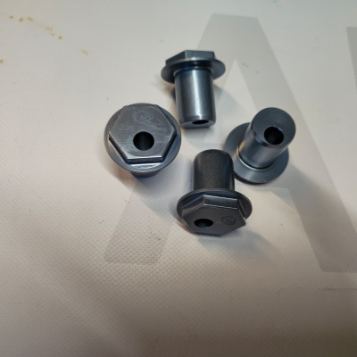 Four metallic bolts with hexagonal heads and holes on a white surface