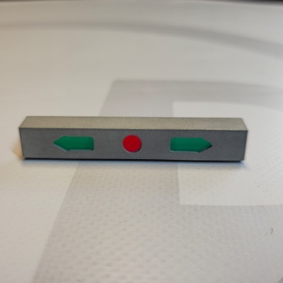 Metallic rectangular object with green arrows and red circle on a white patterned surface