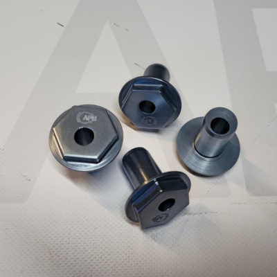 Four metallic hex flange spacers or bolts with central holes on white surface