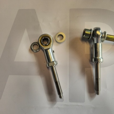 Two metal rod ends with spherical bearings and threaded shafts on a white surface with A P text background