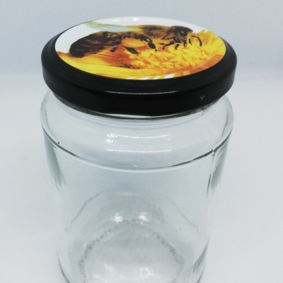 Frasco de vidro com tampa preta e imagem de abelha numa flor amarela.