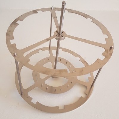 Estrutura metálica circular com aros perfurados apoiada em superfície branca