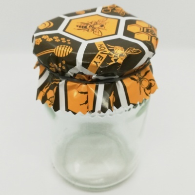 Frasco de vidro com tampa decorada com padrão de abelhas e texto HONEY