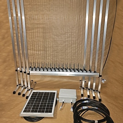 Estrutura metálica com lâminas transparentes, painel solar e cabos sobre superfície castanha