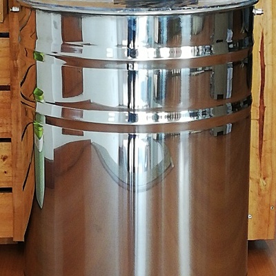 Dispositivo cilíndrico metálico com manivela vermelha e torneira branca sobre chão de madeira