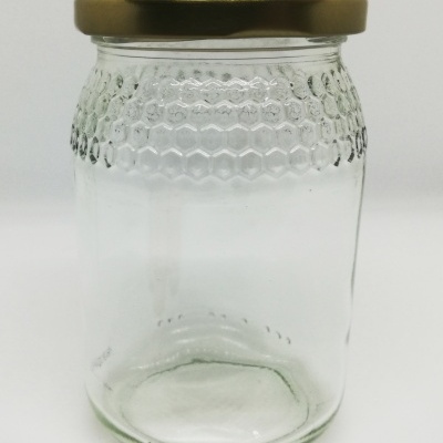 Frasco de vidro transparente com tampa metálica dourada e textura de colmeia