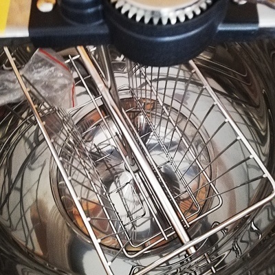 Recipiente metálico com grelha interna e mecanismo manual dentado na borda.