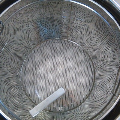 Cesto metálico perfurado redondo com pegas dentro de um recipiente metálico