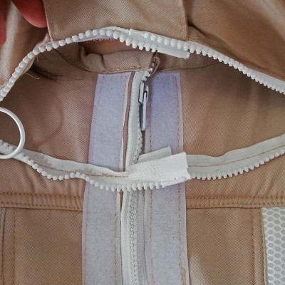 Casaco bege com fecho éclair branco e velcro na parte interna.