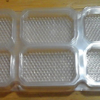 Embalagem plástica transparente com seis compartimentos hexagonais sobre fundo de madeira