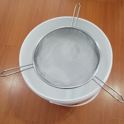 Peneira metálica sobre recipientes brancos em madeira