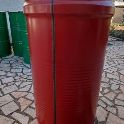 Barril metálico vermelho com rebordo prateado num piso de mosaico exterior.