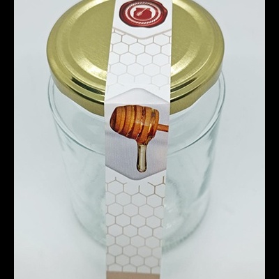 Frasco de vidro com tampa dourada e etiqueta branca com padrão de favos de mel