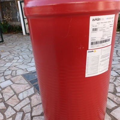 Tambor metálico vermelho com rótulos e texto, em pavimento de mosaico