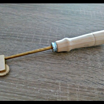 Ferramenta com rodas dentadas de metal e cabo de madeira sobre mesa de madeira escura