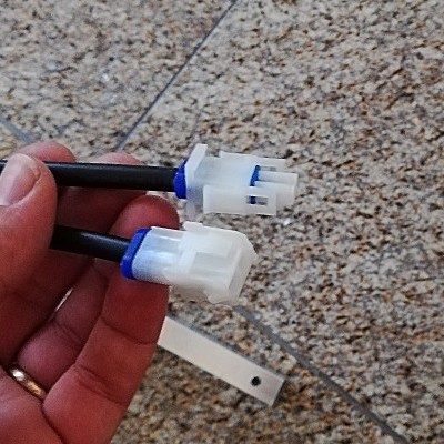 Conector elétrico branco com detalhes azuis e cabos pretos em chão de azulejos