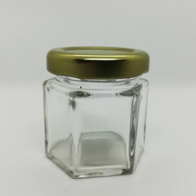 Frasco de vidro hexagonal com tampa dourada sobre fundo branco