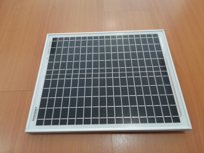 Painel solar quadrado com estrutura branca e células solares pretas sobre chão de madeira.