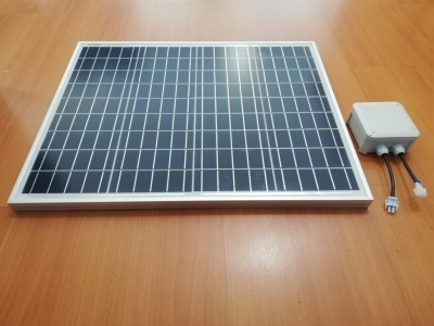 Painel solar azul retangular com moldura branca sobre mesa de madeira, ao lado caixa branca com cabos