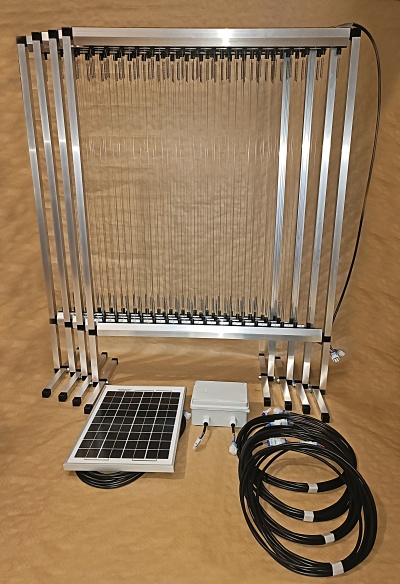 Estrutura metálica com lâminas transparentes, painel solar e cabos sobre superfície castanha