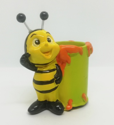 Figura decorativa de abelha amarela junto a recipiente verde com detalhes laranja