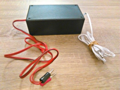 Caixa eletrónica preta com cabos vermelho e branco sobre mesa de madeira