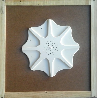 Objeto branco em forma de flor com oito pétalas sobre superfície castanha e moldura de madeira