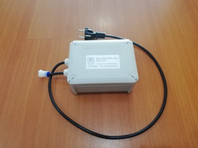 Caixa eletrónica cinza com cabos pretos e ficha elétrica sobre madeira clara