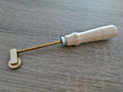 Ferramenta com rodas dentadas de metal e cabo de madeira sobre mesa de madeira escura