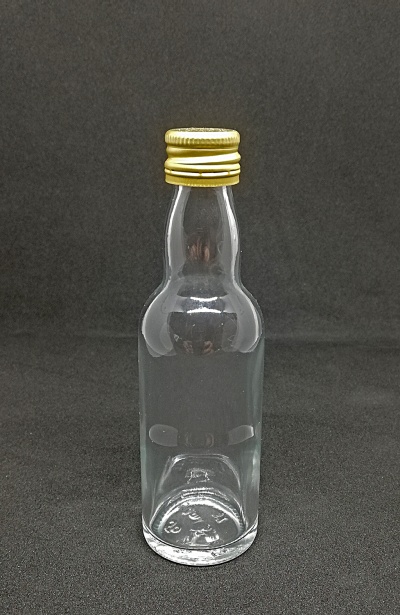 Garrafa de vidro transparente com tampa dourada sobre fundo preto