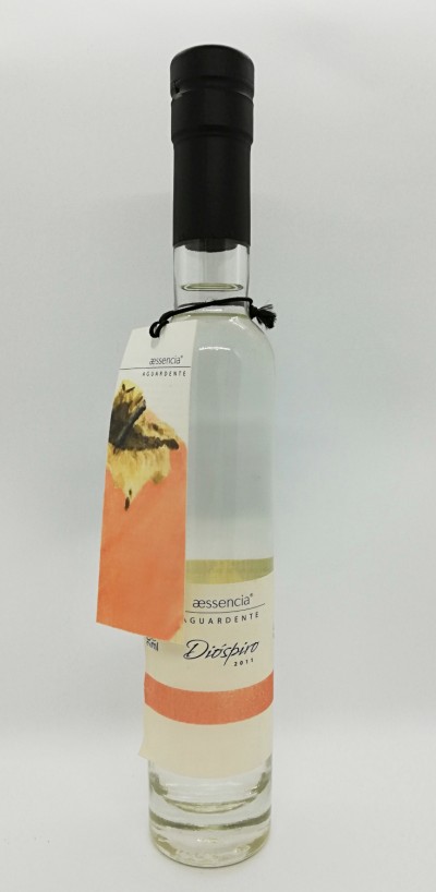 Garrafa de aguardente clara com rótulo Aessencia Diospiro 2011 e etiqueta pendurada com imagem de fruto