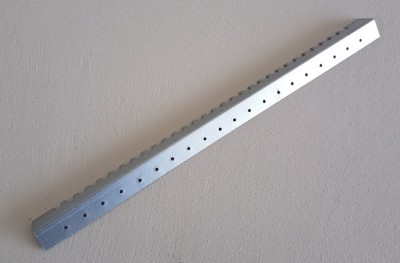 Barra metálica perfurada prateada sobre superfície cinzenta