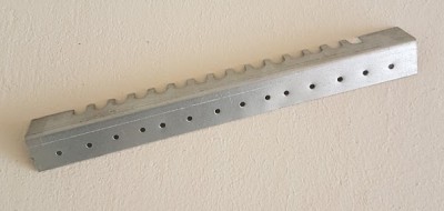 Suporte metálico prateado fosco com orifícios e ondulações sobre superfície bege