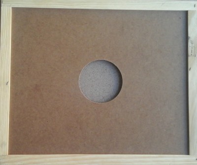 Parte traseira de um quadro com moldura de madeira e painel castanho com orifício circular