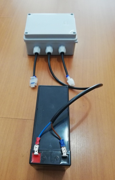 Caixa branca com cabos e bateria preta sobre mesa de madeira