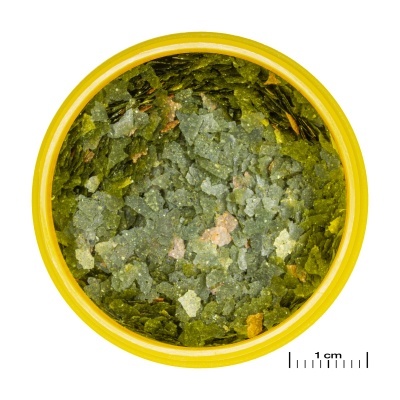 Frasco amarelo aberto com flocos verdes e castanhos granulados dentro.