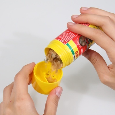 Frasco de tempero vermelho e amarelo a ser despejado na tampa por duas mãos