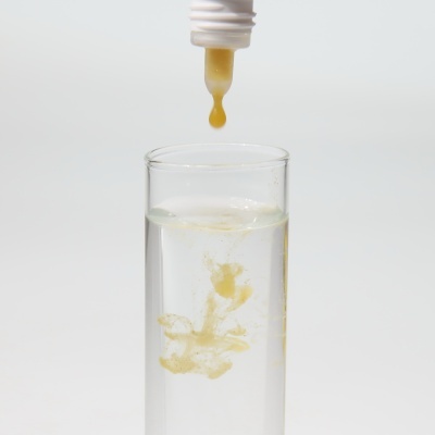 Tubo a gotear líquido amarelo num copo de vidro com líquido transparente