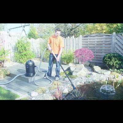 Jovem a utilizar equipamento para limpar lago de jardim com plantas e pedras ao redor