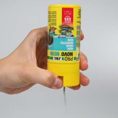 Frasco amarelo de cola ou tinta líquida com etiqueta azul e amarela manuseado por uma mão