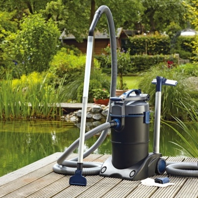 aspirador de piscina preto e azul com mangueira cinza ao lado de piscina natural