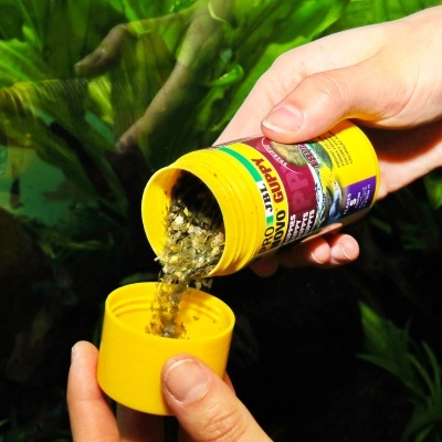 Comida para peixe aquático sendo despejada na tampa amarela da embalagem