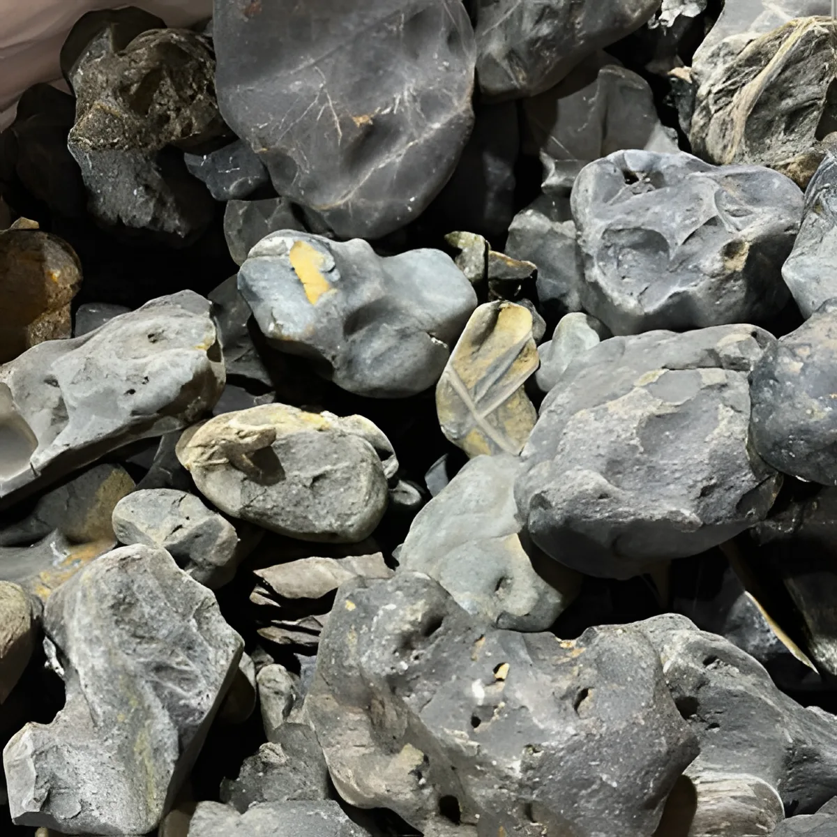 Pedras rugosas cinza com manchas amarelas empilhadas em pilha