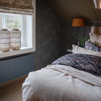 Quarto com cama, almofadas, candeeiro e janelas com estore