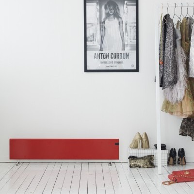 Radiador vermelho numa parede branca com cabideiro branco cheio de casacos e sapatos, quadro preto e branco na parede