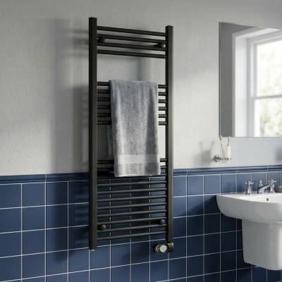 Radiador toalheiro preto com toalha cinzenta, parede branca e azulejos azuis, lavatório branco com espelho